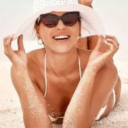 Frau mit Sonnenhut am Strand, perfekt für Gesichtspflegeroutine im Sommer.