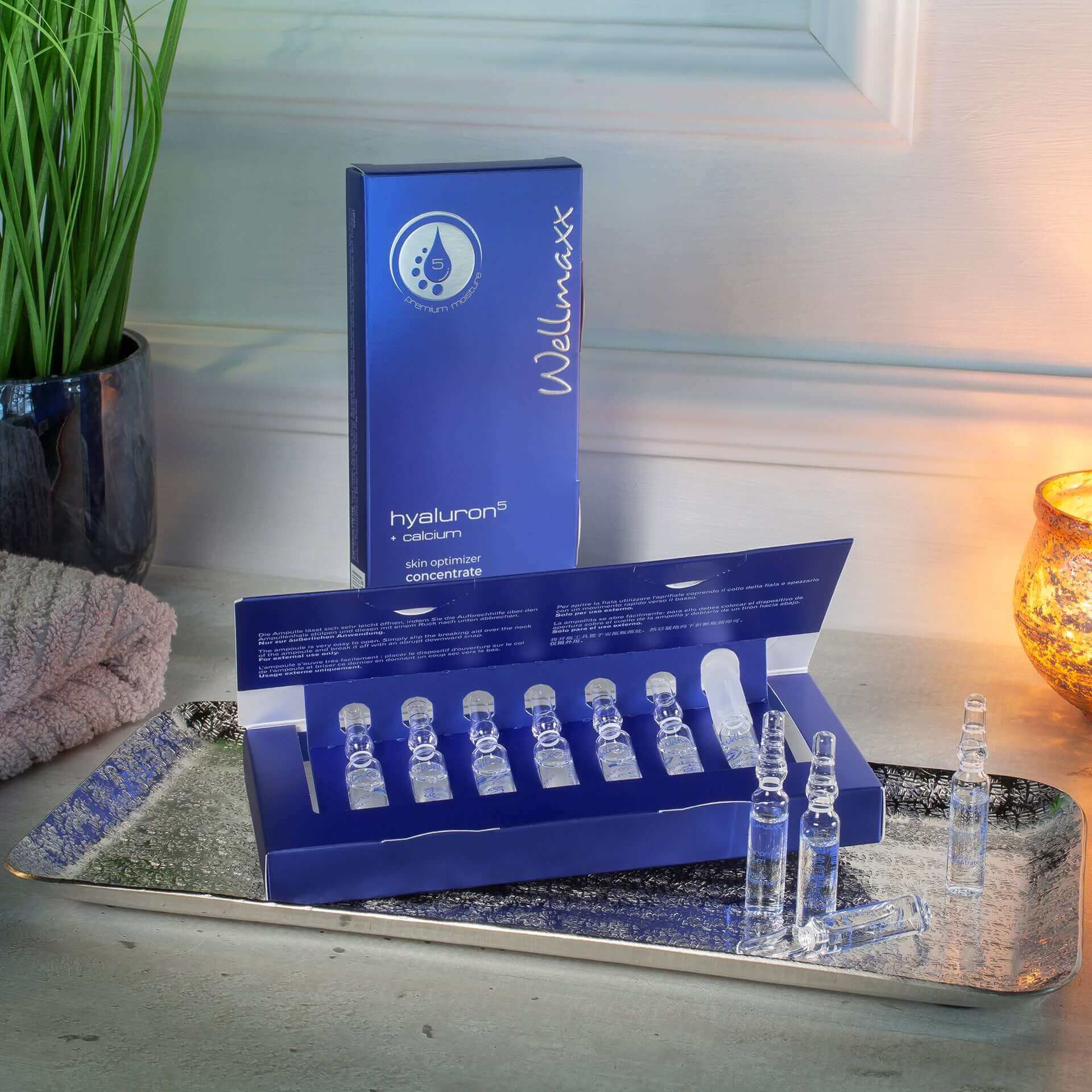 Hyaluronic acid and calcium skin serum in blue packaging, displayed on a silver tray with candles and greenery.