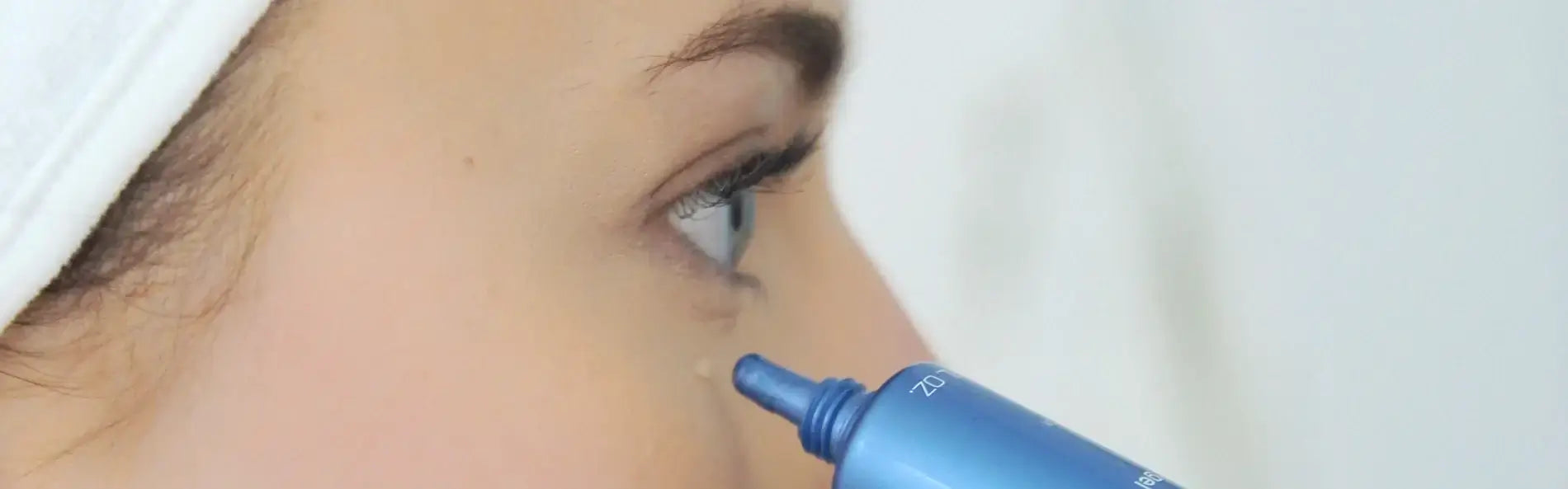 Close-up of a woman applying eye cream with a blue tube, showcasing skincare routine for under-eye area.