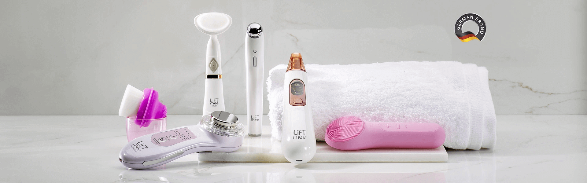 Array of beauty devices on a marble surface, featuring facial tools, scrubbing brushes, and a towel for skincare.