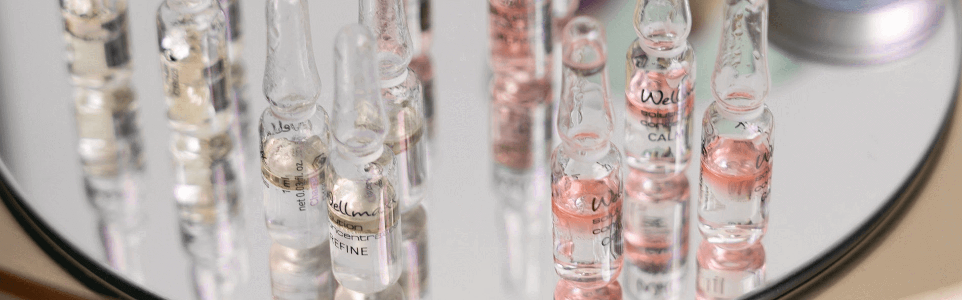 Close-up of glass vials on a mirrored surface, showcasing various skincare formulations in elegant packaging.