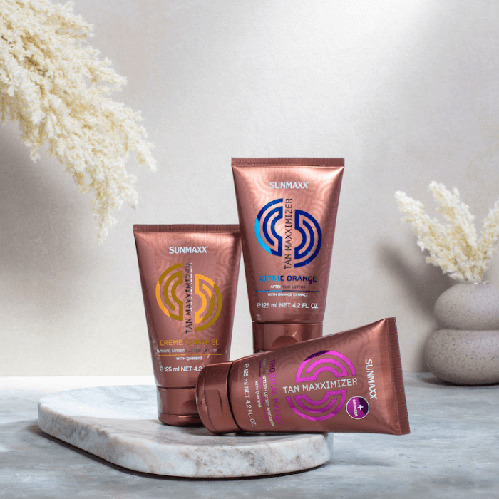 Three Tan Maximizer lotions in colorful tubes on a stone surface, enhancing tanning with tropical scents.