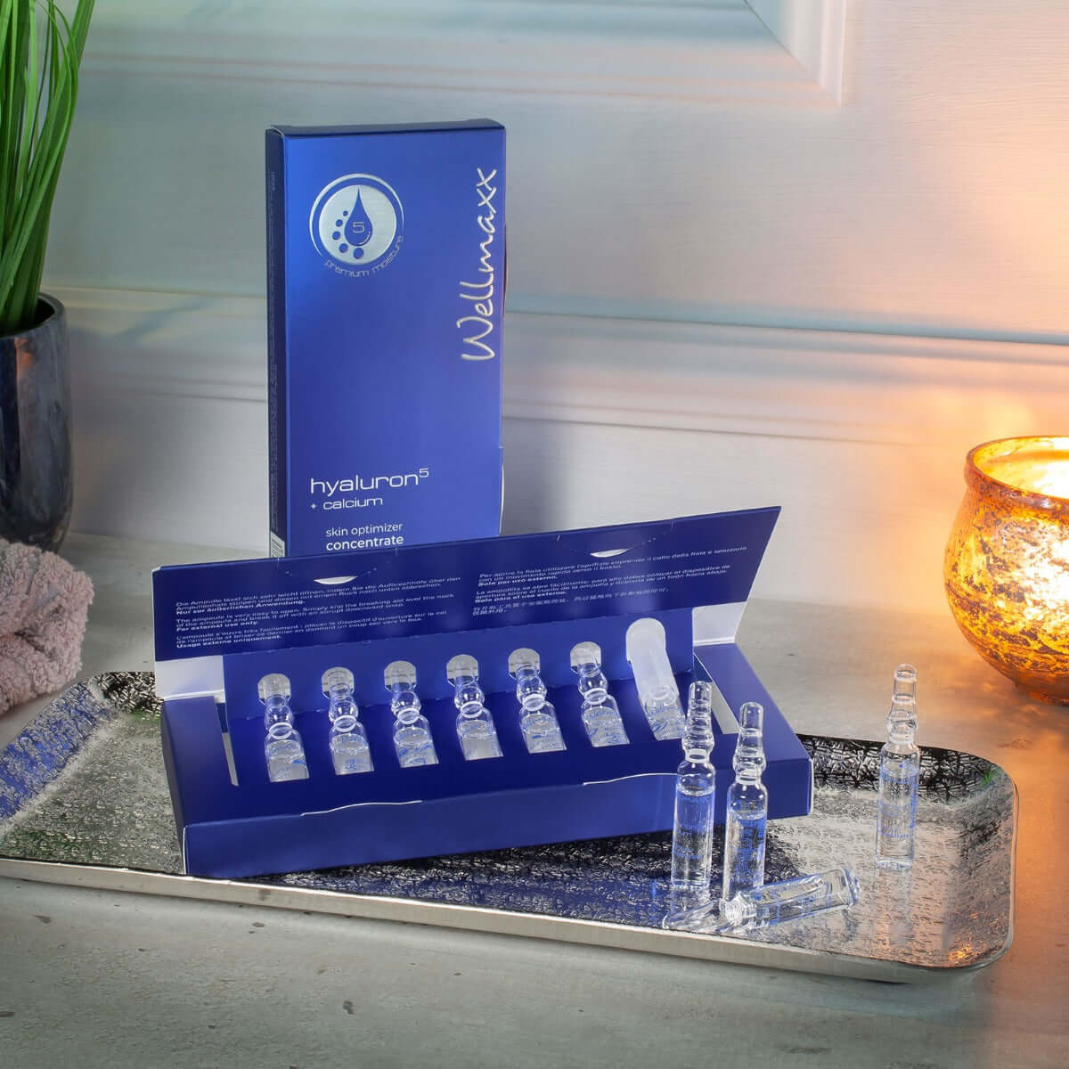 Hyaluron⁵ calcium skin optimizer concentrate in ampoules displayed on a reflective tray with candlelight.