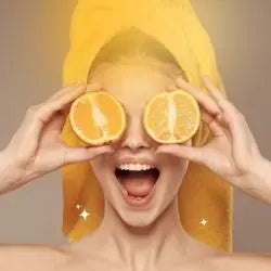 Frau mit Handtuch hält Orangenscheiben vor dem Gesicht, steht für Die besten Vitamin-C Seren.