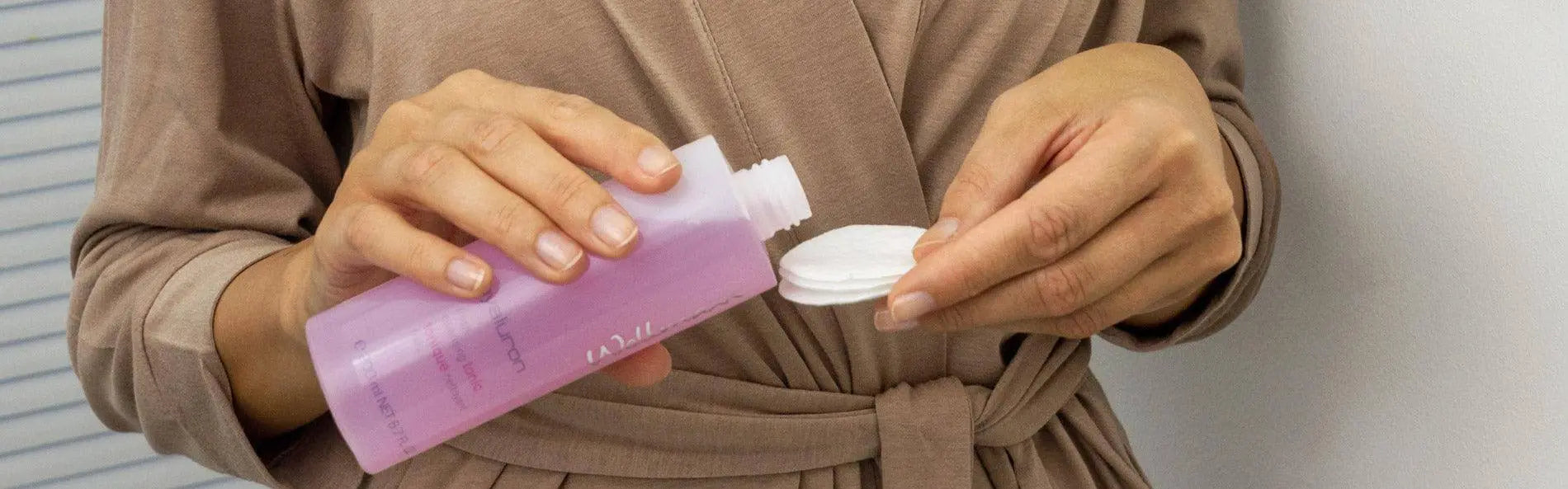 Hände halten eine Flasche mit Gesichtsreinigungsprodukt und Wattepad für die tägliche Reinigung der Haut.