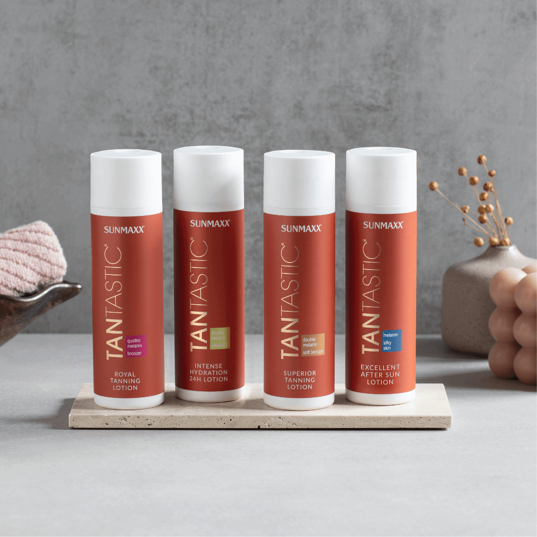 Four bottles of SUNMAXX TANTASTIC tanning lotion and after-sun lotion displayed on a stone tray with a pink towel.